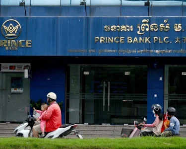 Motorists ride past a branch of the Prince Bank in Phnom Penh on Oct. 15, 2025.