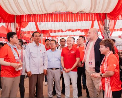 Paulo Gaspar Rodrigues, CEO of Coca-Cola Cambodia Beverage Company, and Charlie Bettencourt, Managing Director of DFI Lucky Private Limited, join H.E. Sreng Hong, Deputy Governor of Battambang Provincial Administration, and H.E. Khlok Noay, Deputy Governor of Banteay Meanchey Provincial Administration, alongside community members including beneficiaries Sla Mat and Uch Pheap, during the Zero Riel Market initiative held in Battambang and Banteay Meanchey ahead of Khmer New Year 2026.